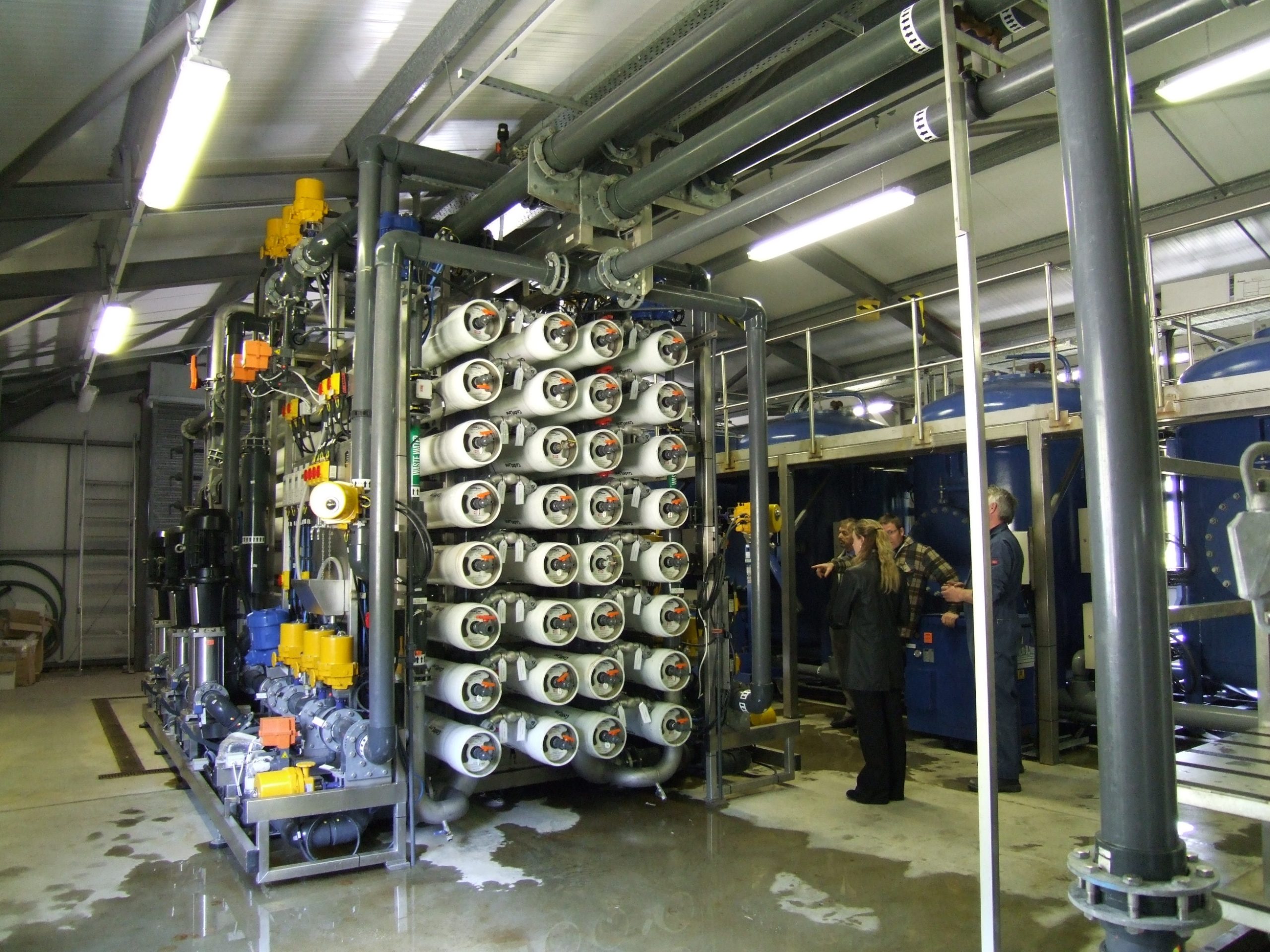 Membrane rig - Scottish Water Image showing water treatment membrane plant with horizontal membrane tubes, and housed in a plant room with people behind. Image shows the difficulty of access to high level equipment