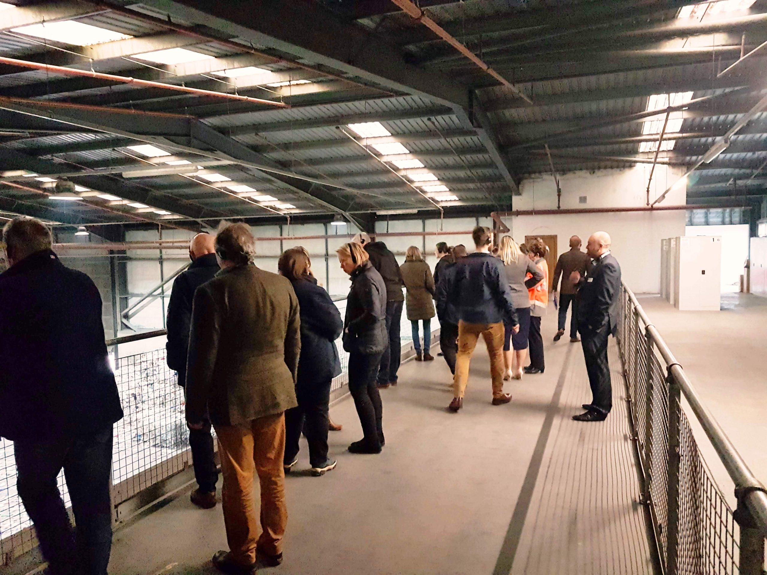 Recycling plant viewing gallery Image shows a floor area with low roof and handrails with members of the public looking over a factory floor.